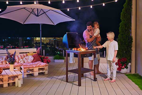 Father holding his daughter and watching his son grill on a small deck at night