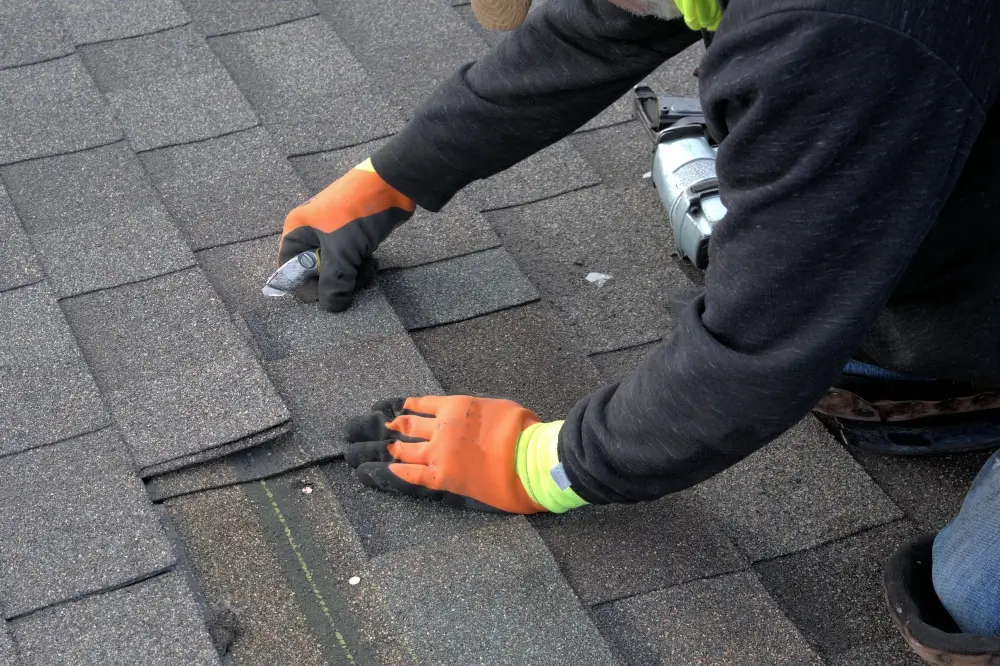 Roofer cuts a shingle to fit during repair work on a residential roof. - Dagmar Construction