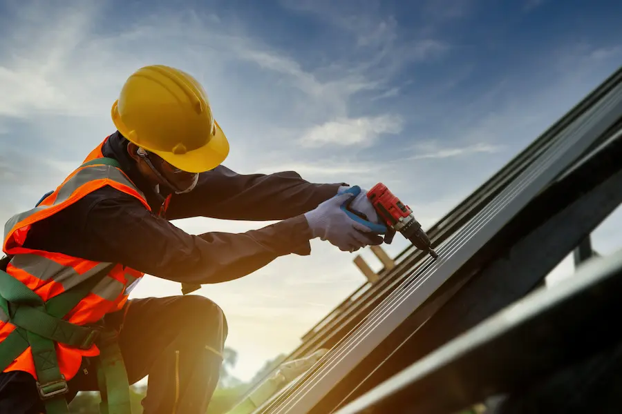 Roofer in protective uniform wear and gloves, installing a new roof with electric drill