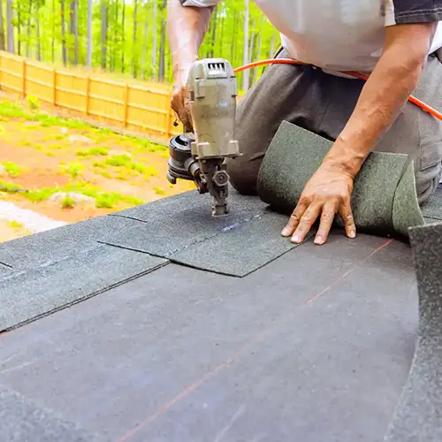 A worker installing asphalt shingles on a residential roof using a nail gun. Ensure your home is protected with expert roofing services from Dagmar Pros LLC