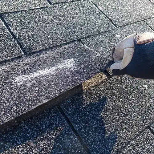 A contractor repairing shingles on a roof, wearing safety gloves and using a utility knife. Keep your roof in top shape with reliable repairs from Dagmar Pros LLC